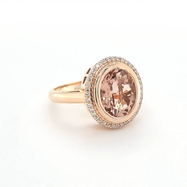 Złoty pierścionek z owalnym morganitem w centrum, otoczony przez halo diamentów na białym tle